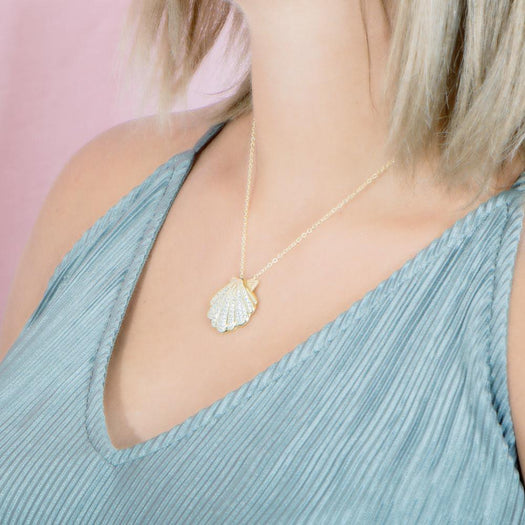The picture shows a model wearing a 925 sterling silver, yellow gold-vermeil, pavé oyster shell pendant with topaz.