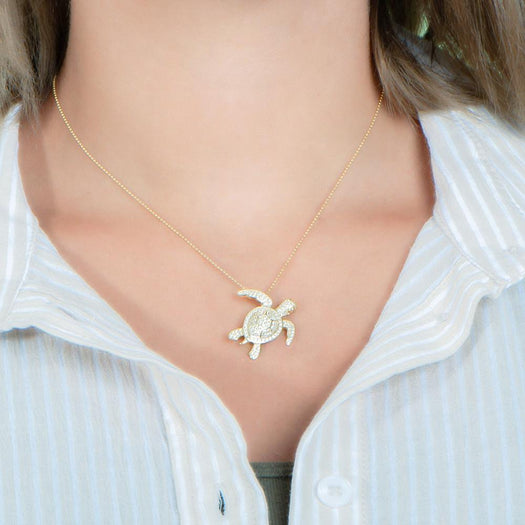 The picture shows a model wearing a 925 sterling silver yellow gold vermeil sea turtle pendant with cubic zirconia.