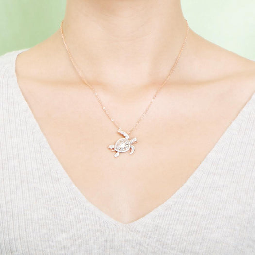 The picture shows a model wearing a 925 sterling silver rose gold vermeil sea turtle pendant with cubic zirconia.