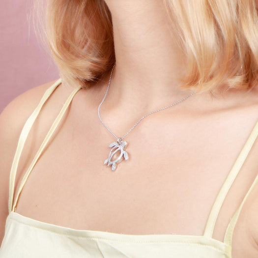 In this photo there is a model with blonde hair and a yellow shirt turned to the left, wearing a white gold sea turtle pendant with topaz gemstones.