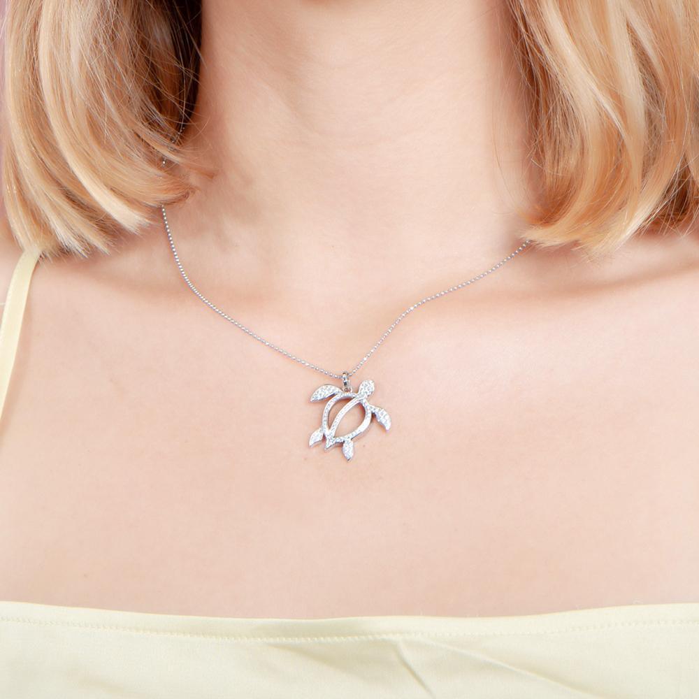 In this photo there is a model with blonde hair and a yellow shirt, wearing a white gold sea turtle pendant with topaz gemstones.