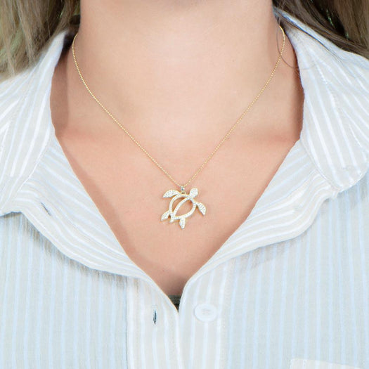 In this photo there is a model with blonde hair and a tan and white striped shirt, wearing a yellow gold sea turtle pendant with topaz gemstones.