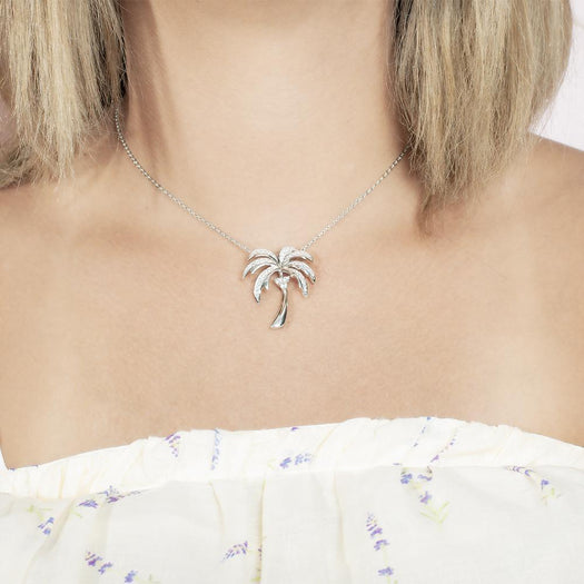 In this photo there is a model with blonde hair and a white shirt with flowers, wearing a white gold palm tree pendant with topaz gemstones.