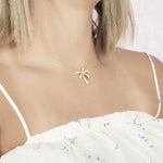 In this photo there is a model turned slightly to the right with blonde hair and a white shirt with flowers, wearing a yellow gold palm tree pendant with topaz gemstones.