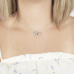 In this photo there is a model with blonde hair and a white shirt with flowers, wearing a white gold palm tree pendant with topaz gemstones.