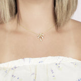 In this photo there is a model with blonde hair and a white shirt with flowers, wearing a yellow gold palm tree pendant with topaz gemstones.