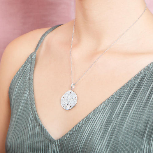 The picture shows a model wearing a large 925 sterling silver, white gold vermeil, pavé sand dollar pendant with topaz.