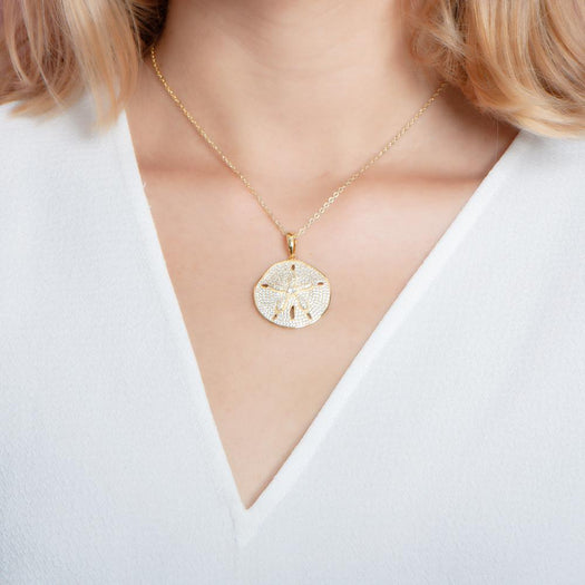 The picture shows a model wearing a large 925 sterling silver, yellow gold vermeil, pavé sand dollar pendant with topaz.