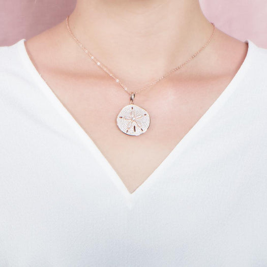 The picture shows a model wearing a large 925 sterling silver, rose gold vermeil, pavé sand dollar pendant with topaz.