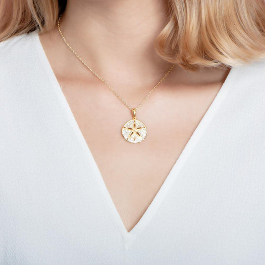 The picture shows a model wearing a medium 925 sterling silver, yellow gold vermeil, pavé sand dollar pendant with topaz.