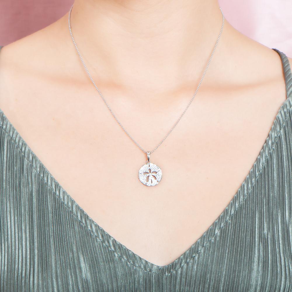 The picture shows a model wearing a small 925 sterling silver, white gold vermeil, pavé sand dollar pendant with topaz.