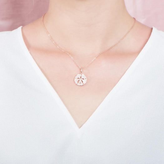 The picture shows a model wearing a small 925 sterling silver, rose gold vermeil, pavé sand dollar pendant with topaz.