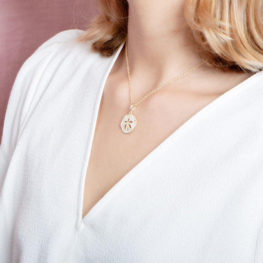 The picture shows a model wearing a small 925 sterling silver, yellow gold vermeil, pavé sand dollar pendant with topaz.