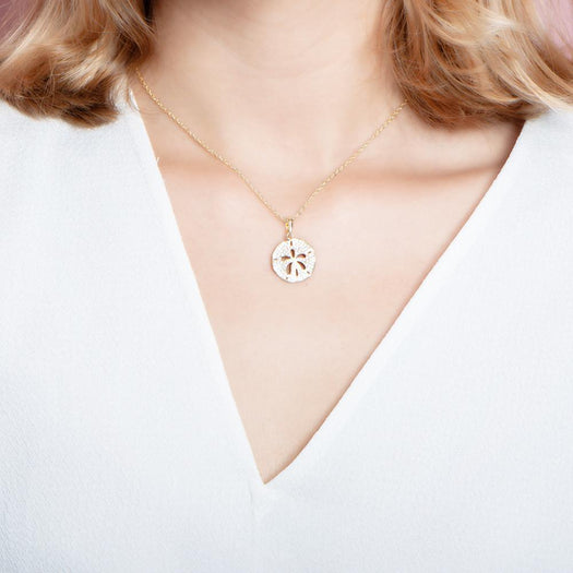 The picture shows a model wearing a small 925 sterling silver, yellow gold vermeil, pavé sand dollar pendant with topaz.