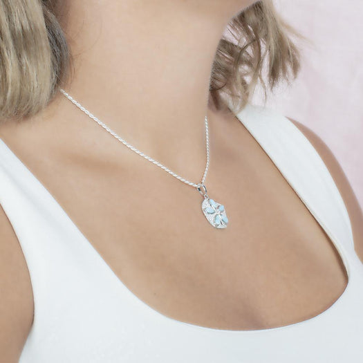 The picture shows a model wearing a 925 sterling silver pavé sand dollar pendant with larimar and topaz.