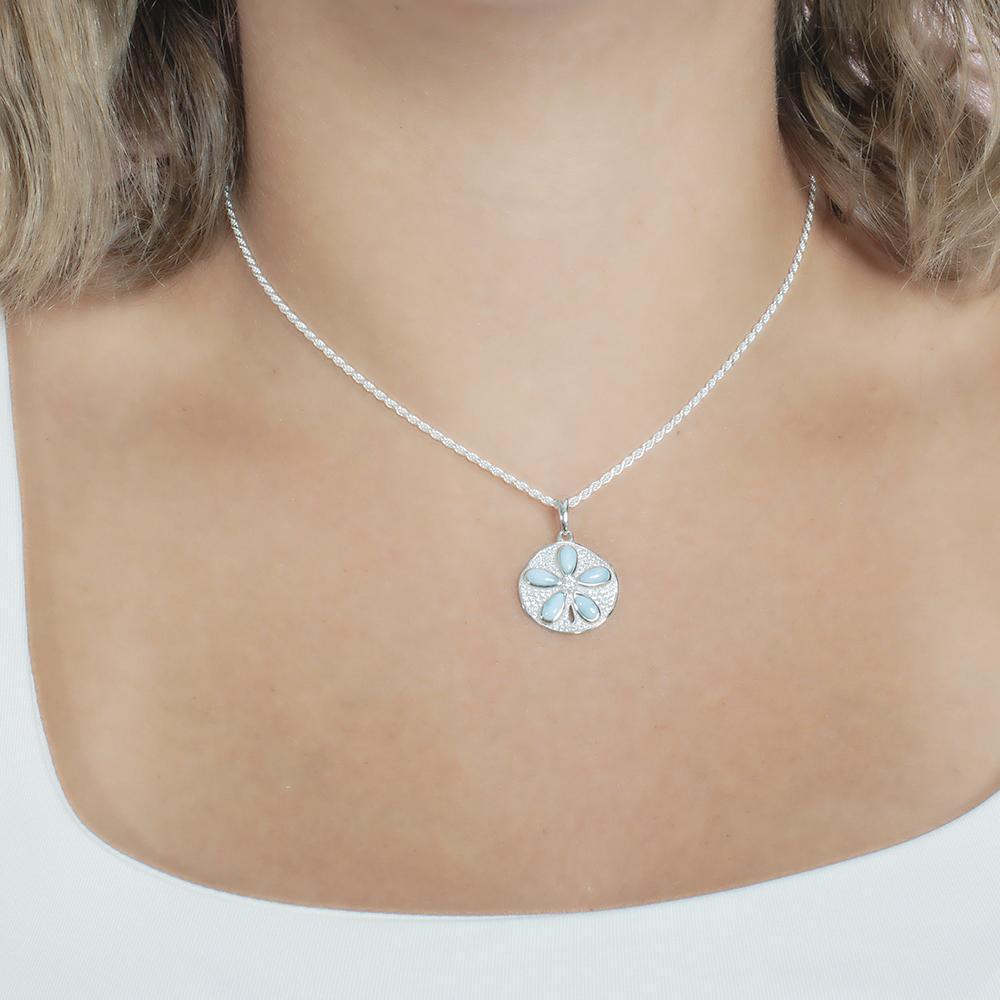 The picture shows a model wearing a 925 sterling silver pavé sand dollar pendant with larimar and topaz.