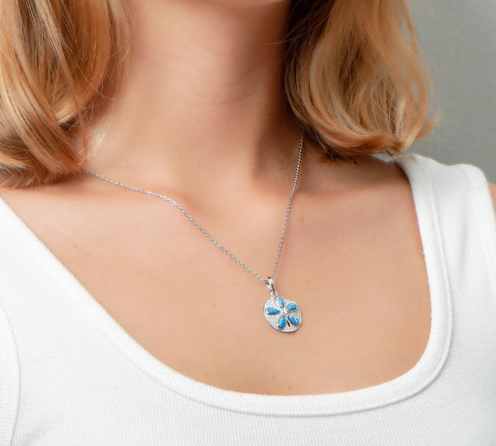 The picture shows a model wearing a 925 sterling silver pavé sand dollar pendant with opalite and topaz.