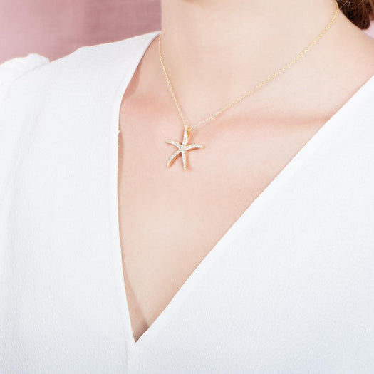 The picture shows a model wearing a 925 sterling silver, yellow gold vermeil, sea star pendant with topaz.