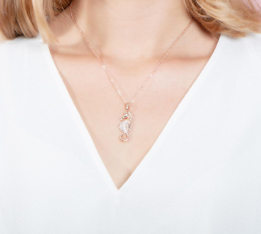 The picture shows a model wearing a 925 sterling silver, rose gold vermeil, pavé seahorse pendant with topaz.