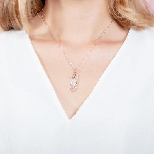 The picture shows a model wearing a 925 sterling silver, rose gold vermeil, pavé seahorse pendant with topaz.