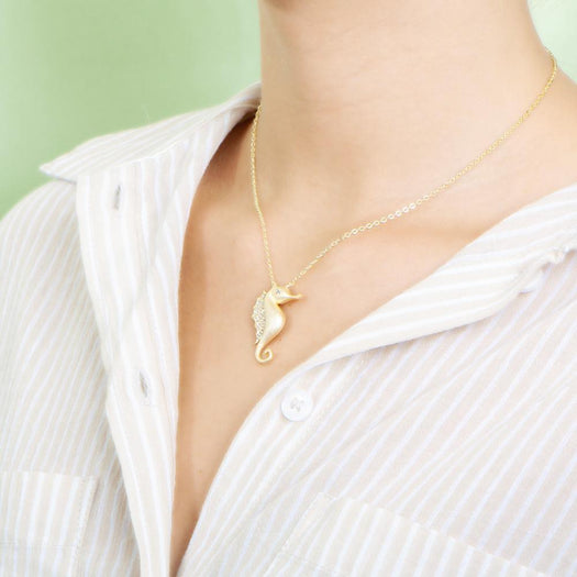 The picture shows a model wearing a 925 sterling silver, yellow gold vermeil, pavé seahorse pendant with topaz.