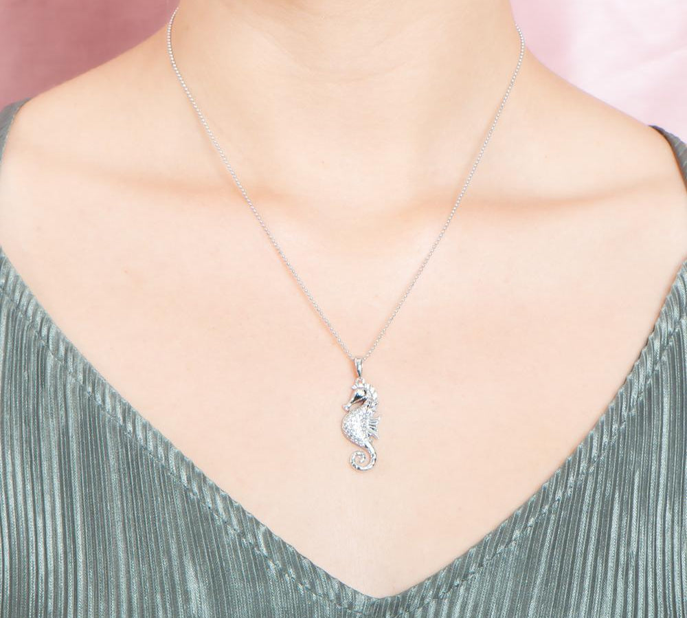 The picture shows a model wearing a 925 sterling silver, white gold vermeil, pavé seahorse pendant with topaz.
