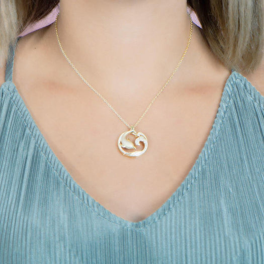 The picture shows a model wearing a 925 sterling silver, yellow gold vermeil, dolphin and wave pendant with topaz.
