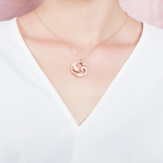 The picture shows a model wearing a 925 sterling silver, rose gold vermeil, dolphin and wave pendant with topaz.