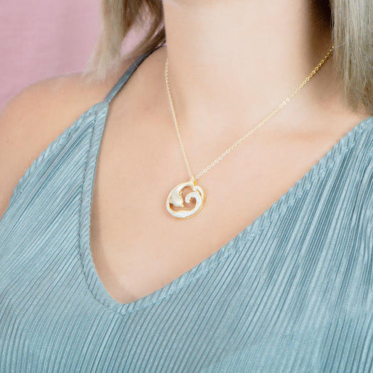 The picture shows a model wearing a 925 sterling silver, yellow gold vermeil, dolphin and wave pendant with topaz.