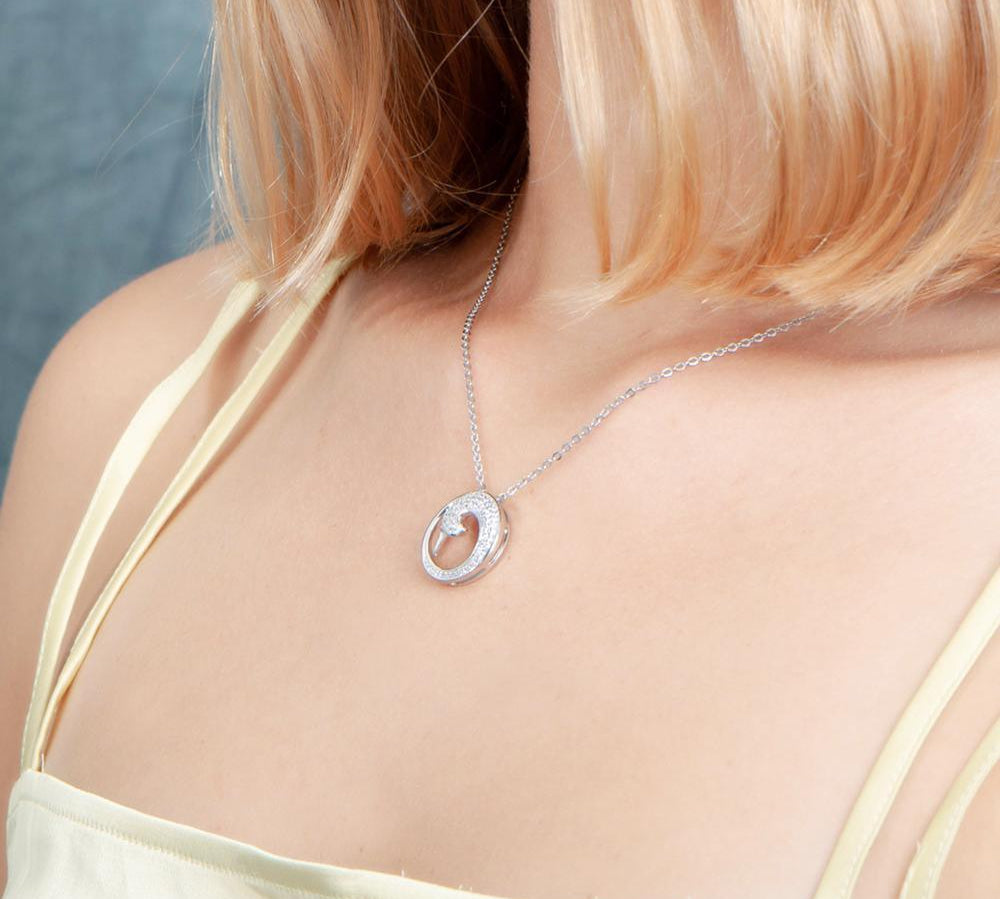 The photo is shows a model wearing a sterling silver pavé wave pendant with topaz.