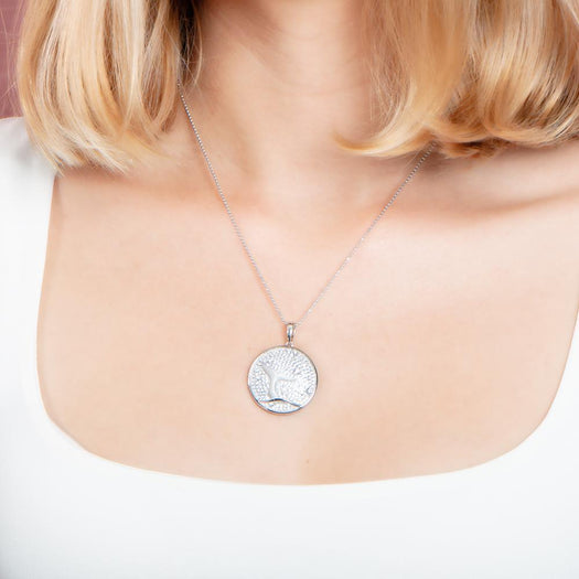 The picture shows a model wearing a 925 sterling silver, white gold vermeil, pavé whale tail medallion pendant with topaz.