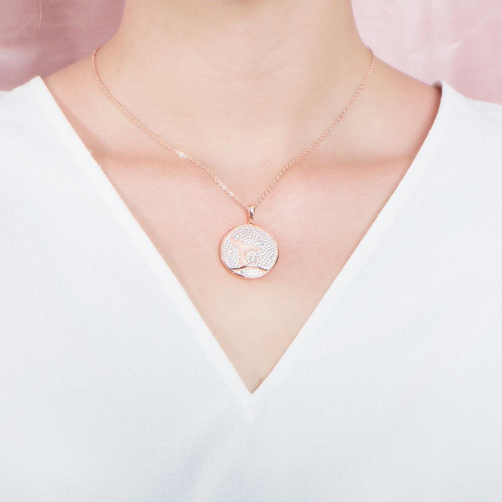 The picture shows a model wearing a 925 sterling silver, rose gold vermeil, pavé whale tail medallion pendant with topaz.