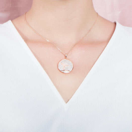 The picture shows a model wearing a 925 sterling silver, rose gold vermeil, pavé whale tail medallion pendant with topaz.