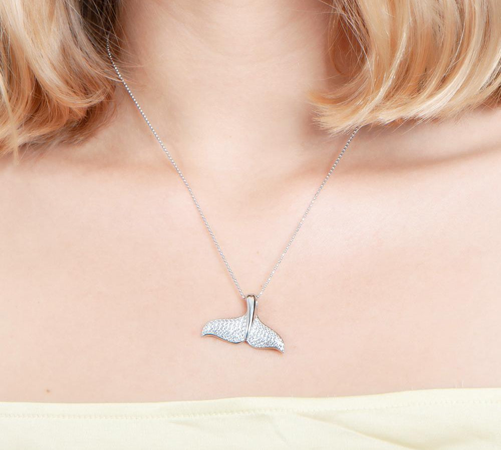 The picture shows a model wearing a 925 sterling silver, white gold vermeil, pavé whale tail pendant with topaz.