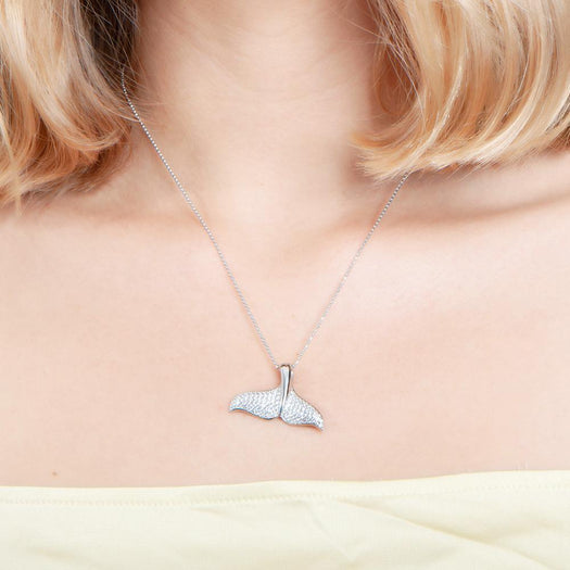 The picture shows a model wearing a 925 sterling silver, white gold vermeil, pavé whale tail pendant with topaz.