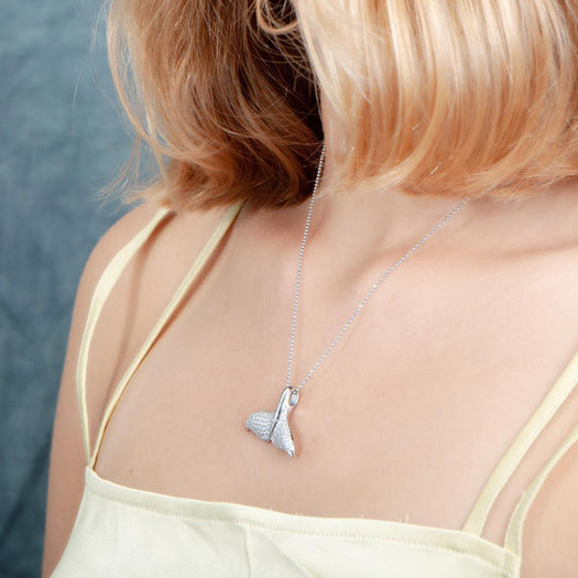 The picture shows a model wearing a 925 sterling silver, white gold vermeil, pavé whale tail pendant with topaz.
