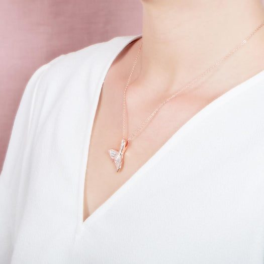 The picture shows a model wearing a 925 sterling silver, rose gold vermeil, pavé whale tail pendant with topaz.