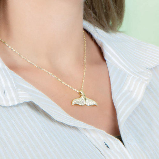 The picture shows a model wearing a 925 sterling silver, yellow gold vermeil, pavé whale tail pendant with topaz.
