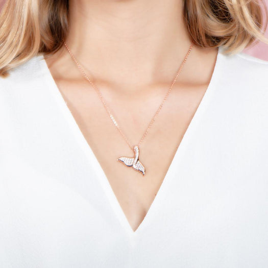 The picture shows a model wearing a 925 sterling silver, rose gold vermeil, pavé whale tail pendant with topaz.