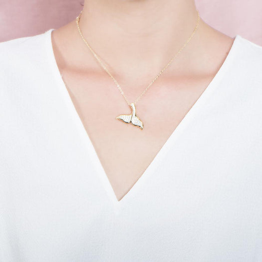 The picture shows a model wearing a 925 sterling silver, yellow gold vermeil, pavé whale tail pendant with topaz.
