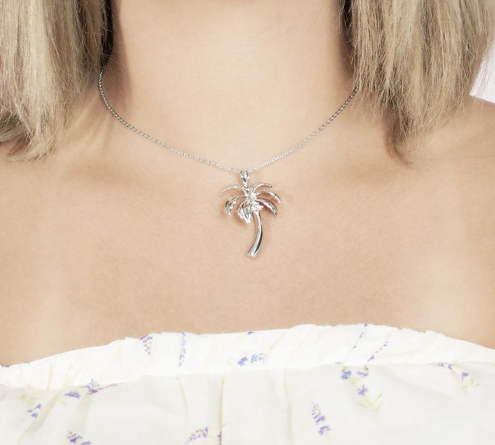 In this photo there is a model with blonde hair and white shirt with purple flowers, wearing a sterling silver palm tree pendant with topaz gemstones.