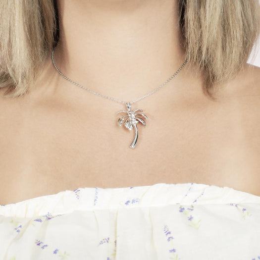 In this photo there is a model with blonde hair and white shirt with purple flowers, wearing a sterling silver palm tree pendant with topaz gemstones.