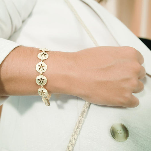 The picture shows a model wearing a yellow gold sand dollar bracelet.