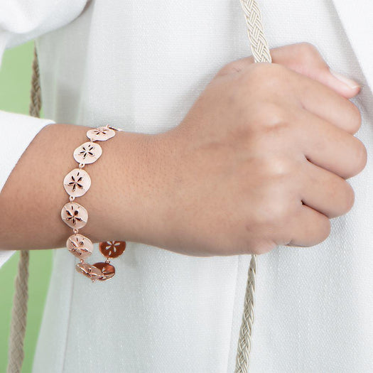 The picture shows a model wearing a rose gold sand dollar bracelet.