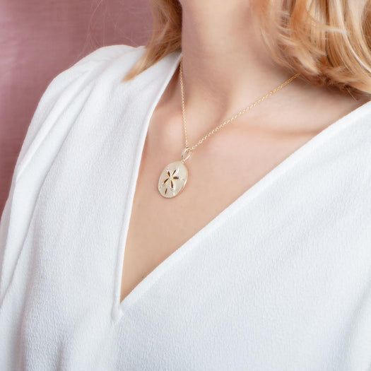 The picture shows a model wearing a yellow gold sand dollar cut out pendant.