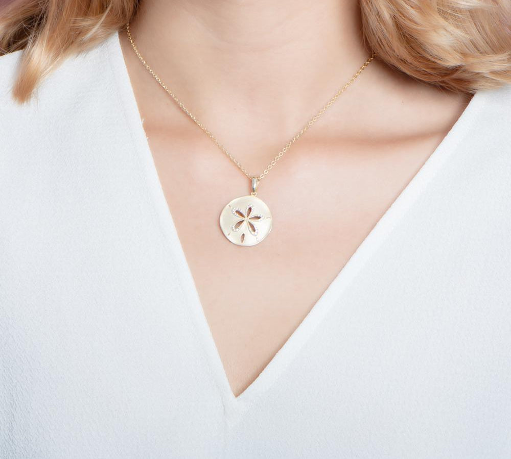 The picture shows a model wearing a yellow gold sand dollar cut out pendant.