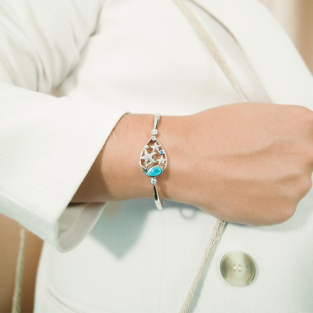The picture shows a model wearing a 925 sterling silver bracelet with three starfish, seaweed, and topaz, aquamarine, and larimar gemstones.