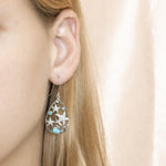 The picture shows a model wearing a sea star larimar earring with topaz and aquamarine gemstones. 