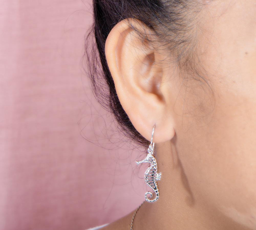 The picture shows a model wearing a 925 sterling silver seahorse hook earring with topaz.