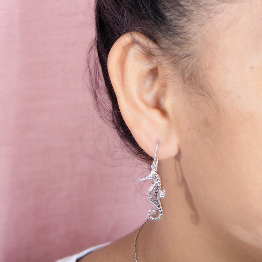 The picture shows a model wearing a 925 sterling silver seahorse hook earring with topaz.